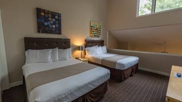 A hotel room with two beds, a nightstand, a lamp, and artwork on the walls.