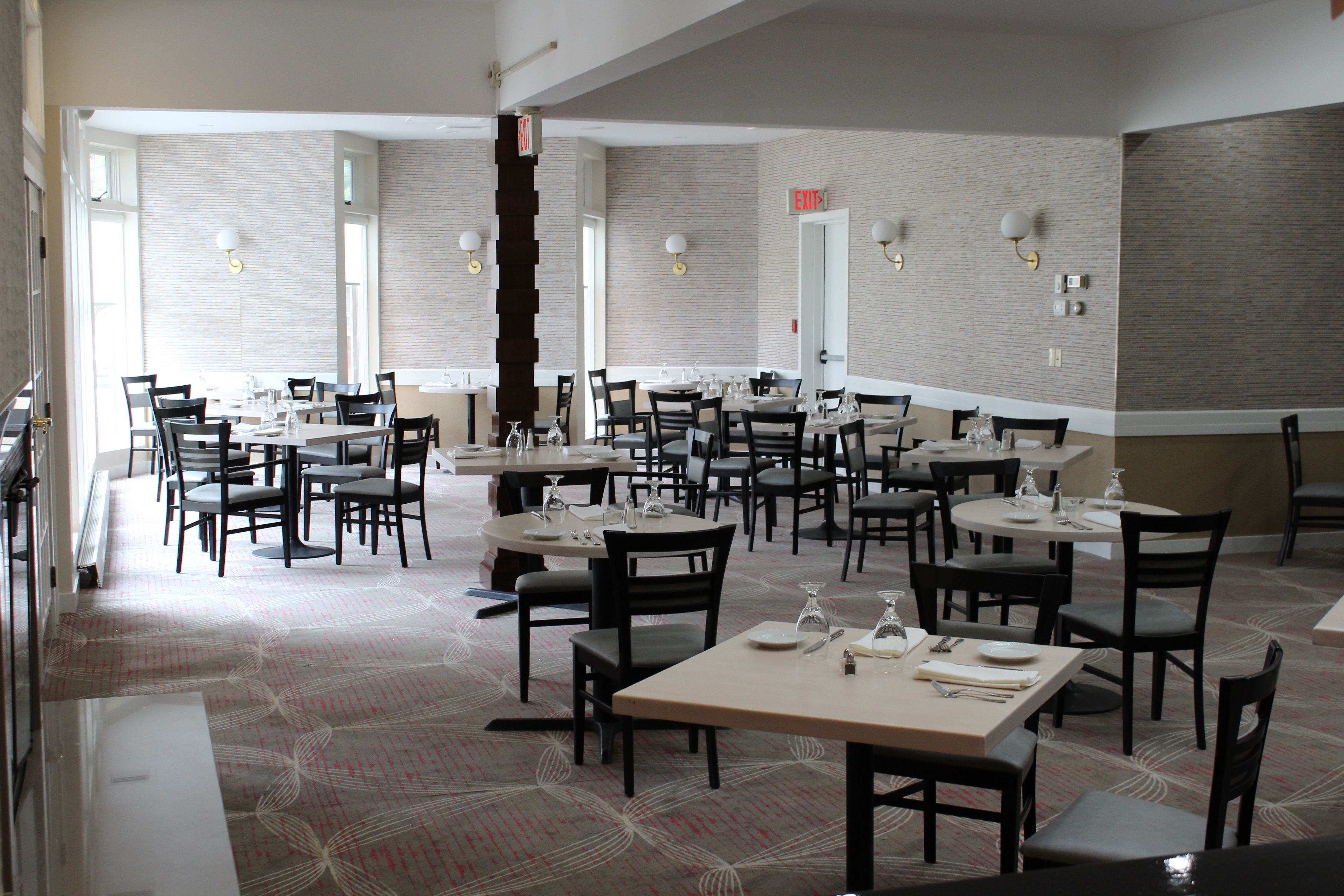 A spacious dining area with multiple tables and chairs, a patterned carpet, and brick walls.
