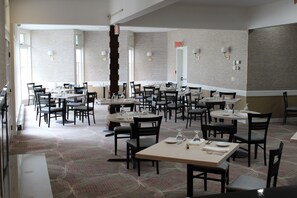 A spacious dining area with multiple tables and chairs, a patterned carpet, and brick walls.