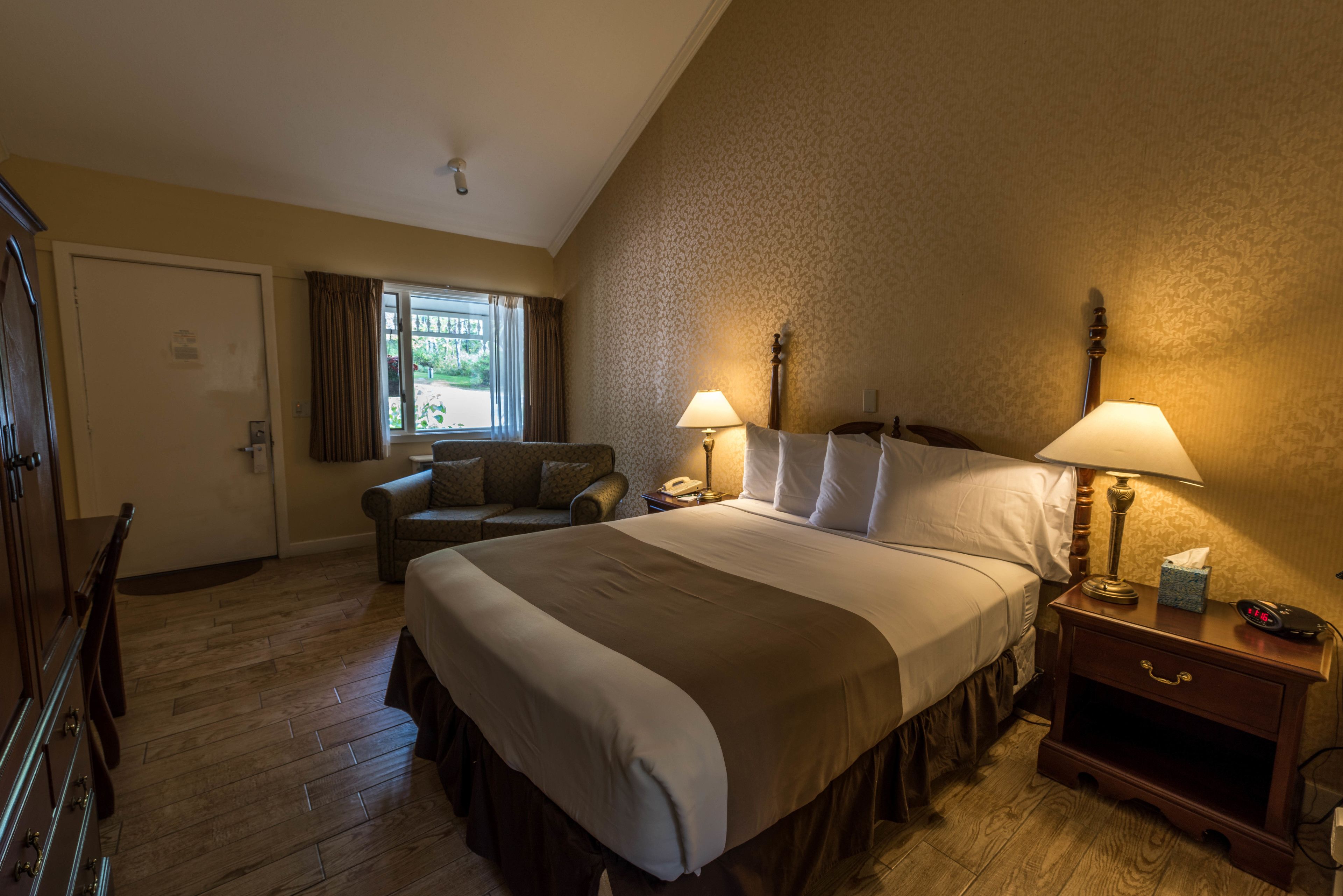 A hotel room with a large bed, two bedside lamps, a nightstand, a chair, and a window with curtains.