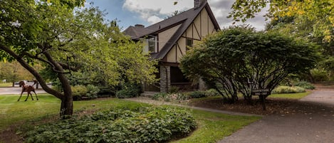 A traditional house with a stone foundation and a gabled roof, surrounded by lush greenery and a well-maintained lawn.