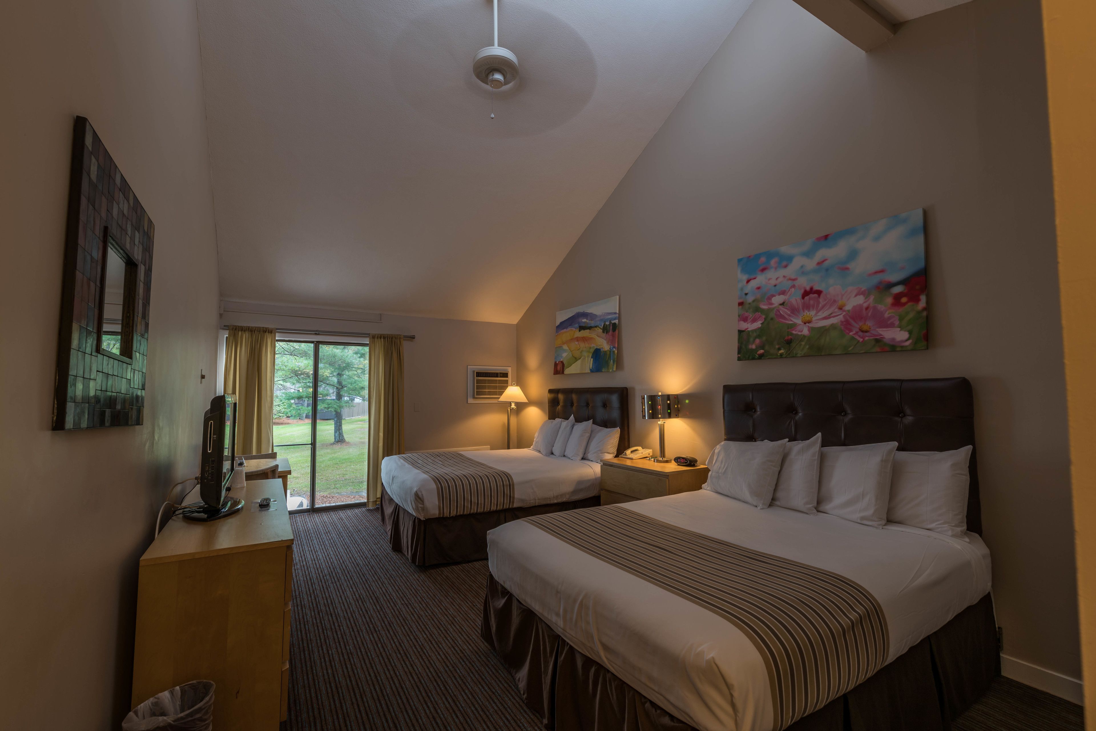 A hotel room with two beds, a desk, a TV, and a painting on the wall.