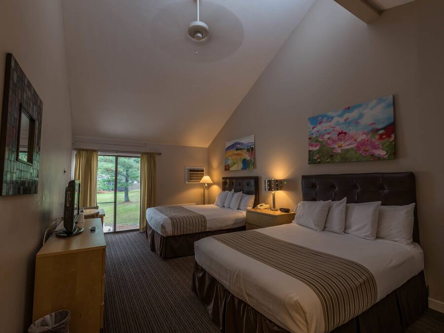 A hotel room with two beds, a desk, a TV, and a painting on the wall.
