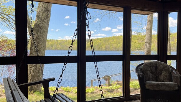 A wooden deck with a swing chair and a bench overlooking a lake. - Interlaken Inn & Resort (Lakeville)