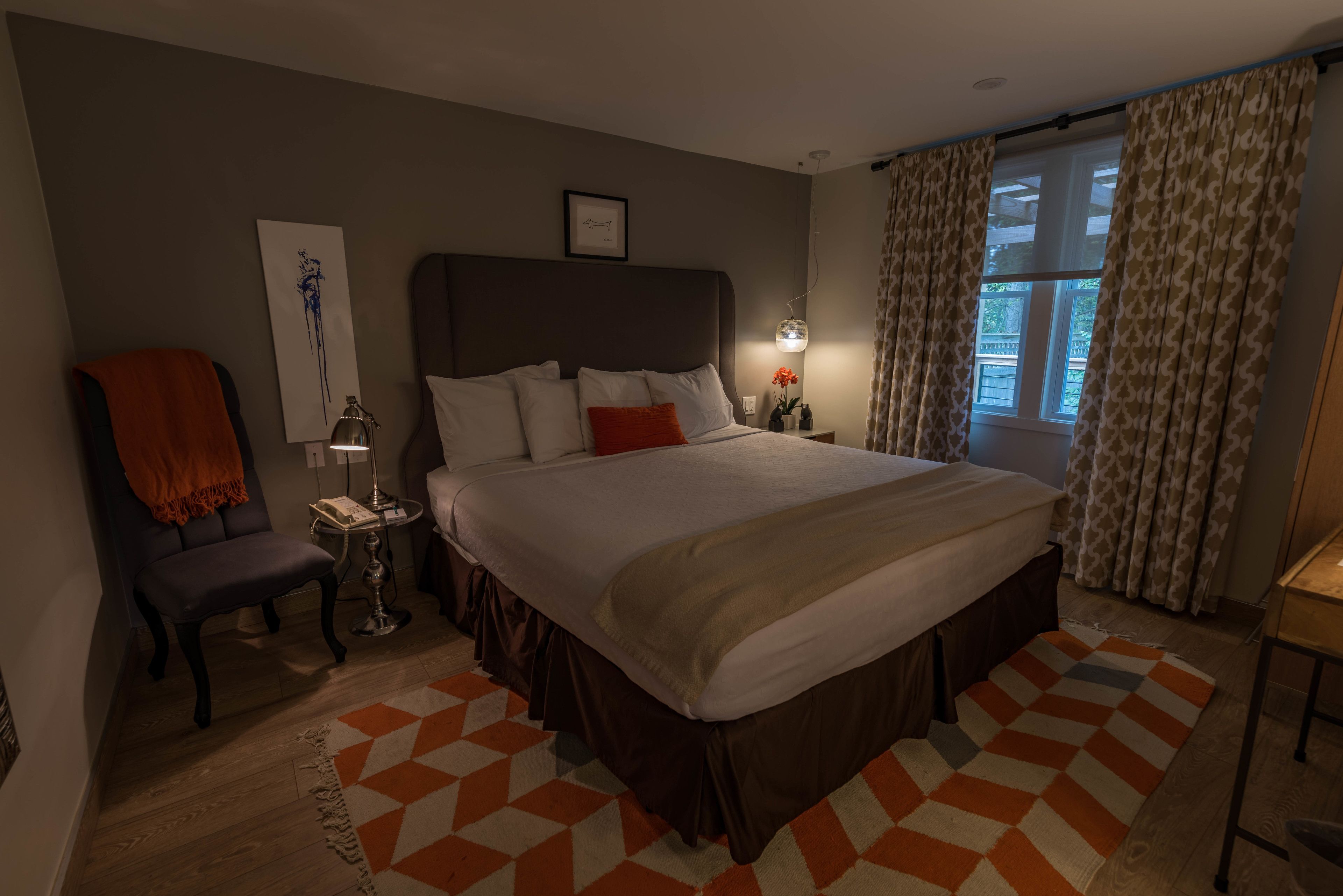 A hotel room with a large bed, a chair, a nightstand, and a window with curtains.