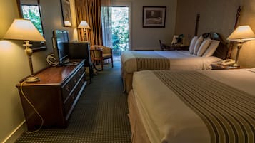 A hotel room with two beds, a television, a dresser, and a desk with a lamp.