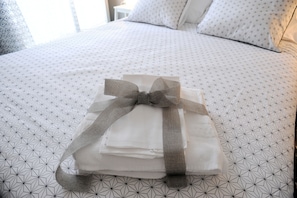 A neatly made bed with a geometric patterned bedspread and a folded white towel with a gray ribbon. - Maison Salerno (Salerno)