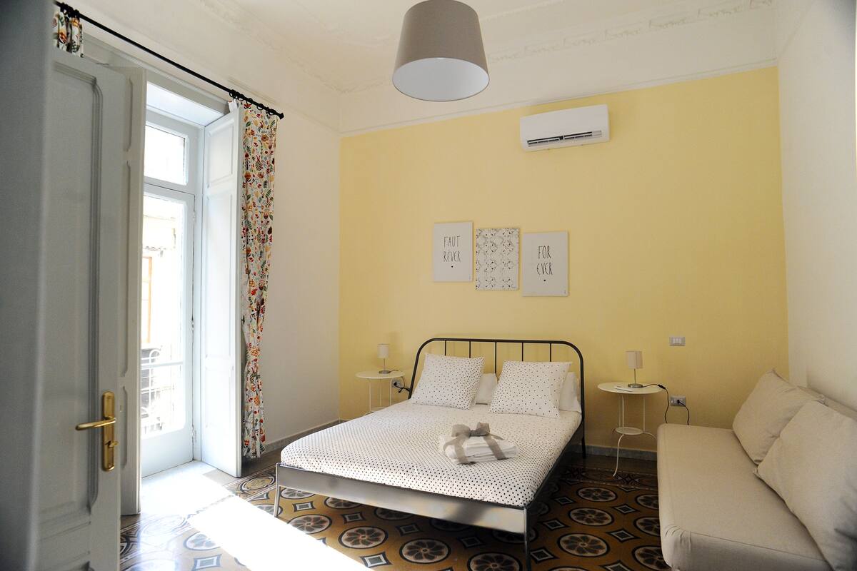 Ein Schlafzimmer mit einem Bett, einer Couch, einem gemusterten Boden und einem Fenster mit Vorhängen.