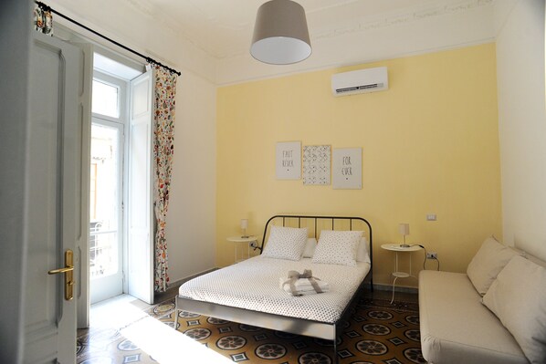 A bedroom with a bed, a sofa, a patterned floor, and a window with curtains. - Maison Salerno (Salerno)