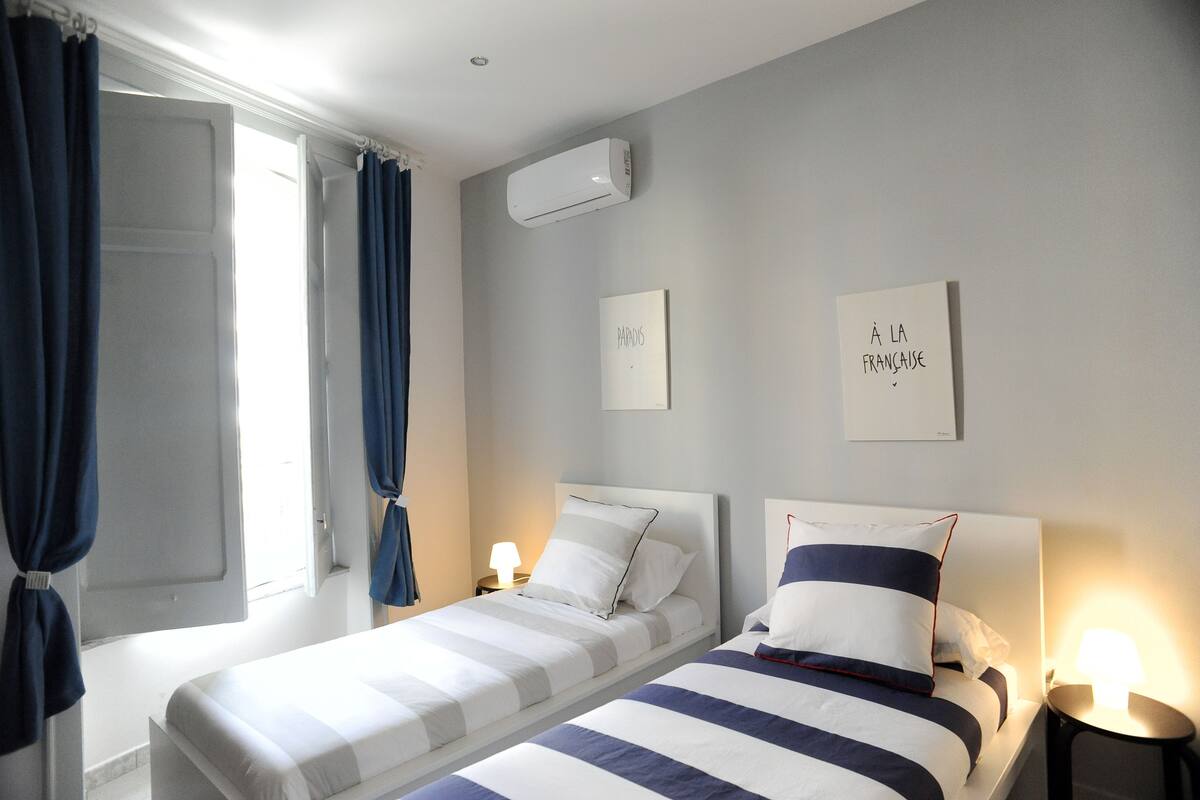 Ein Hotelzimmer mit zwei Betten, einem Vorhangfenster, einer Klimaanlage und Wandbildern.