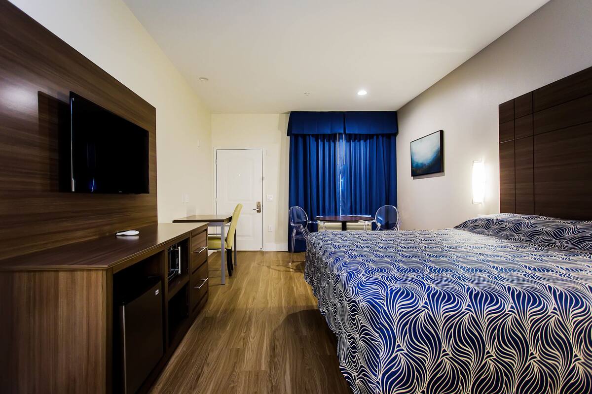 A hotel room with a bed, a desk, a chair, a television, and a window with curtains.