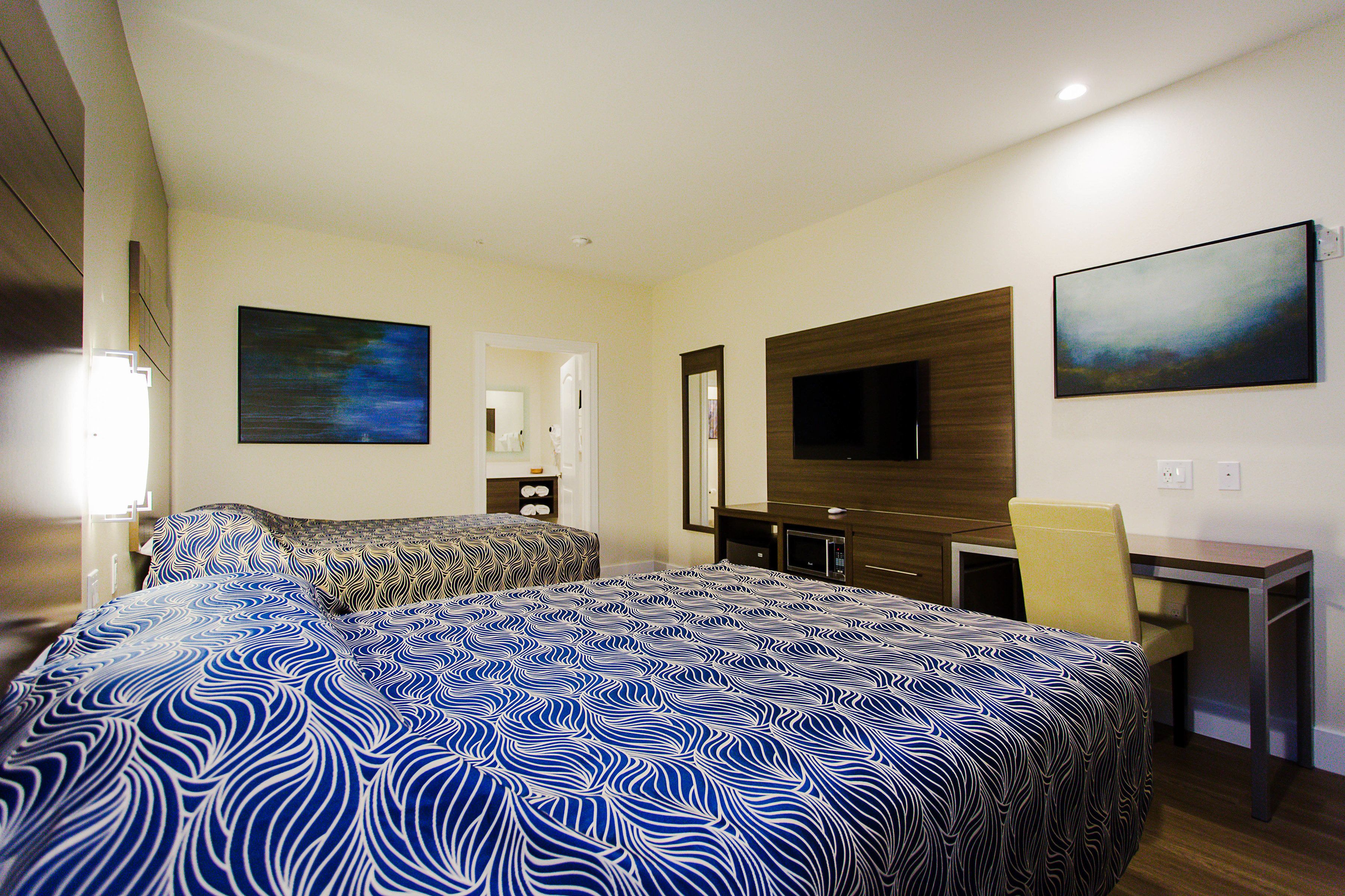 A hotel room with two beds, a desk, a chair, a TV, and artwork on the walls.