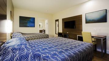 A hotel room with two beds, a desk, a chair, a TV, and artwork on the walls.