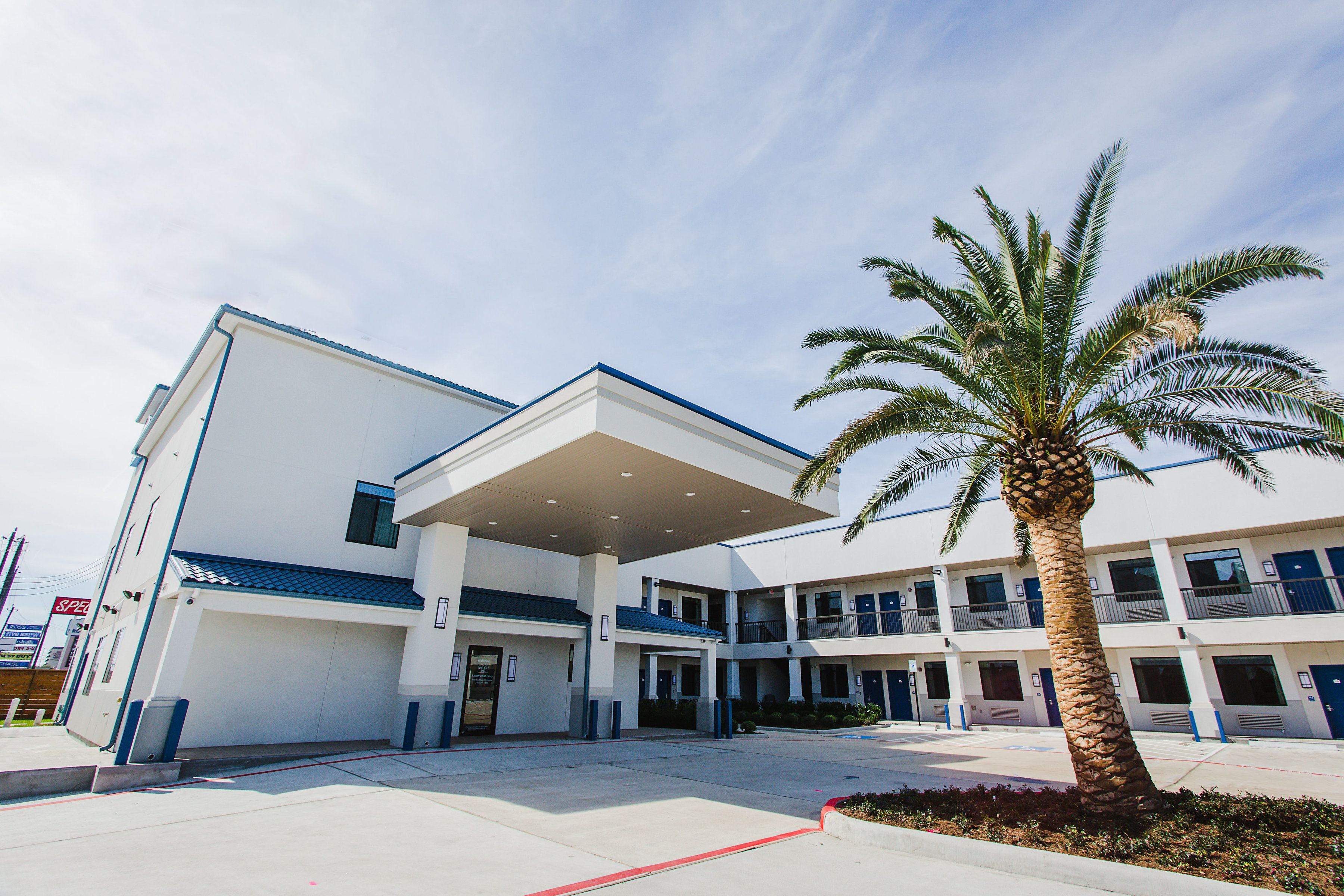 A multi-story building with a covered entrance, a palm tree, and a clear sky.