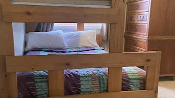 Ein Stockbett mit Holzrahmen, ein unteres Bett mit farbenfroher Bettdecke und eine Kommode mit mehreren Schubladen.