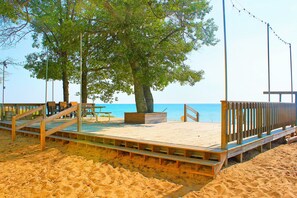 Una terraza de madera con bancos y una mesa de picnic, con vista a una playa arenosa y el océano.