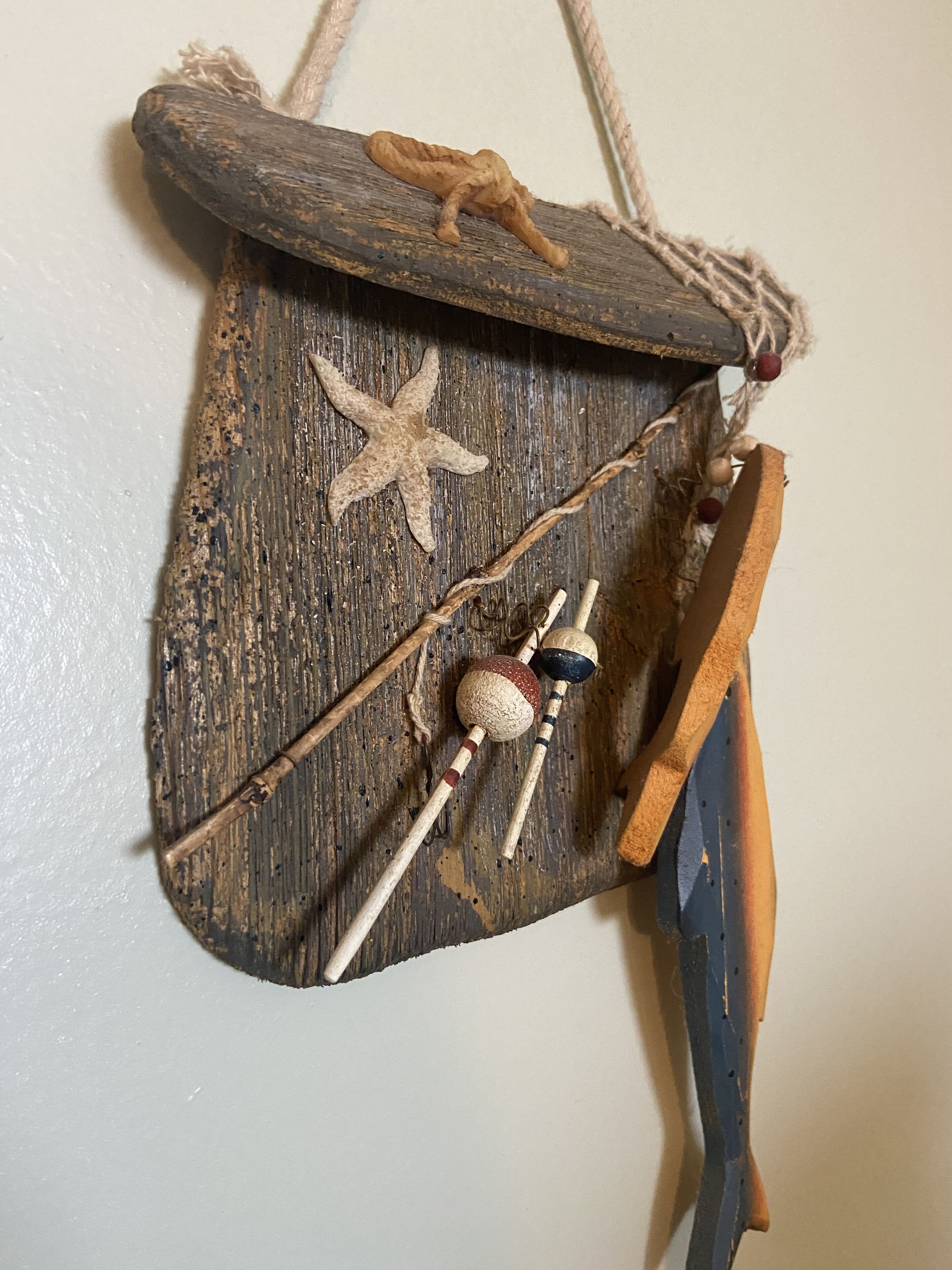 Une décoration murale rustique en bois, ornée d’une étoile de mer, d’une cuillère en bois et d’un petit flacon.