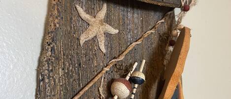 Une décoration murale rustique en bois, ornée d’une étoile de mer, d’une cuillère en bois et d’un petit flacon.