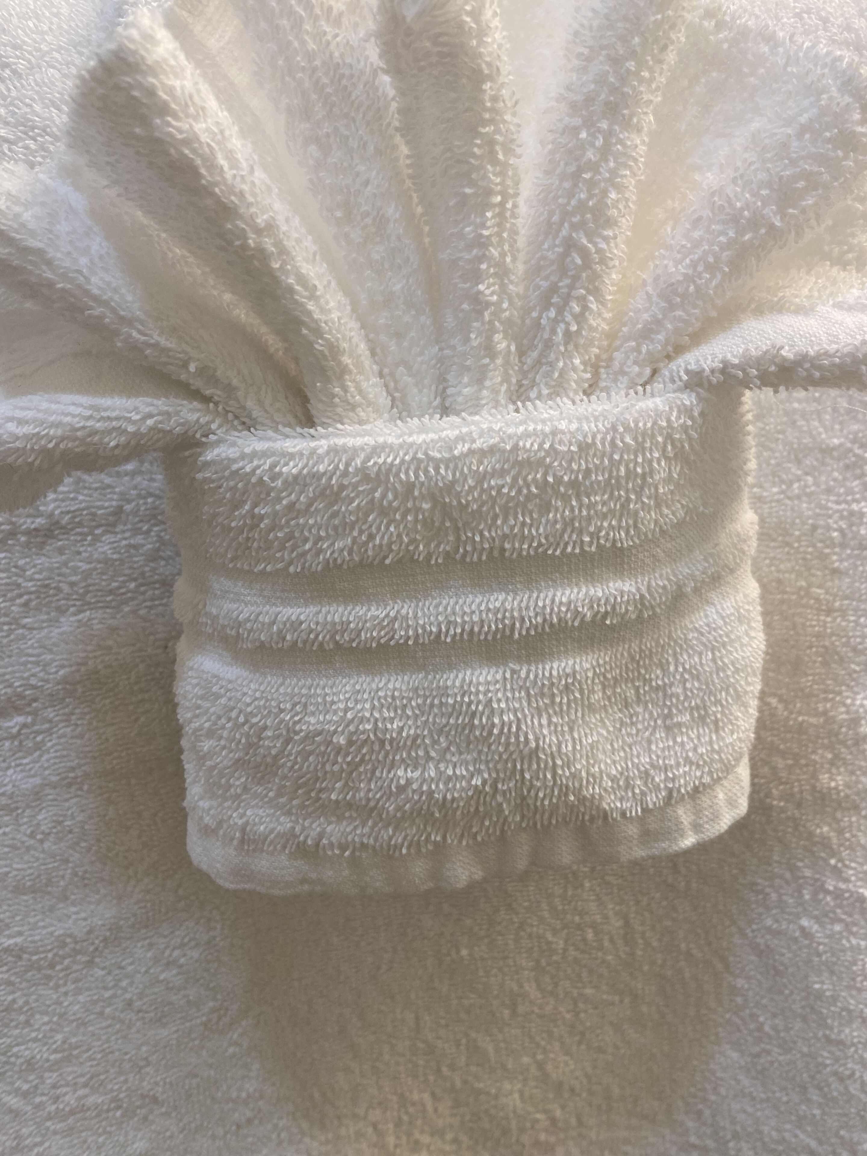 Primer plano de una tela blanca con textura, probablemente una toalla o manta, con un borde ribeteado y un asa anillada.