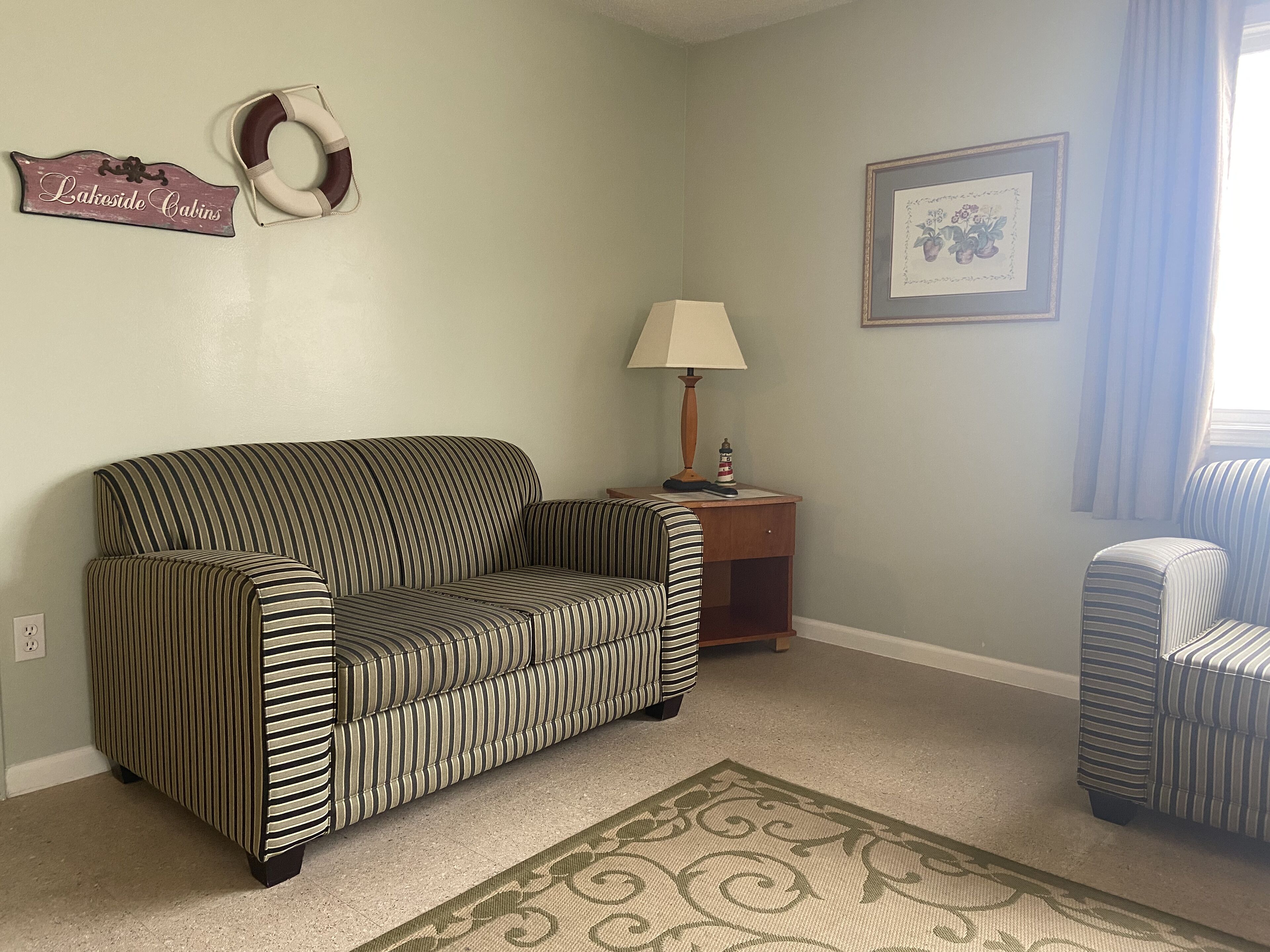 A living room with a striped sofa, a small side table with a lamp, a framed picture on the wall, and a rug on the floor.