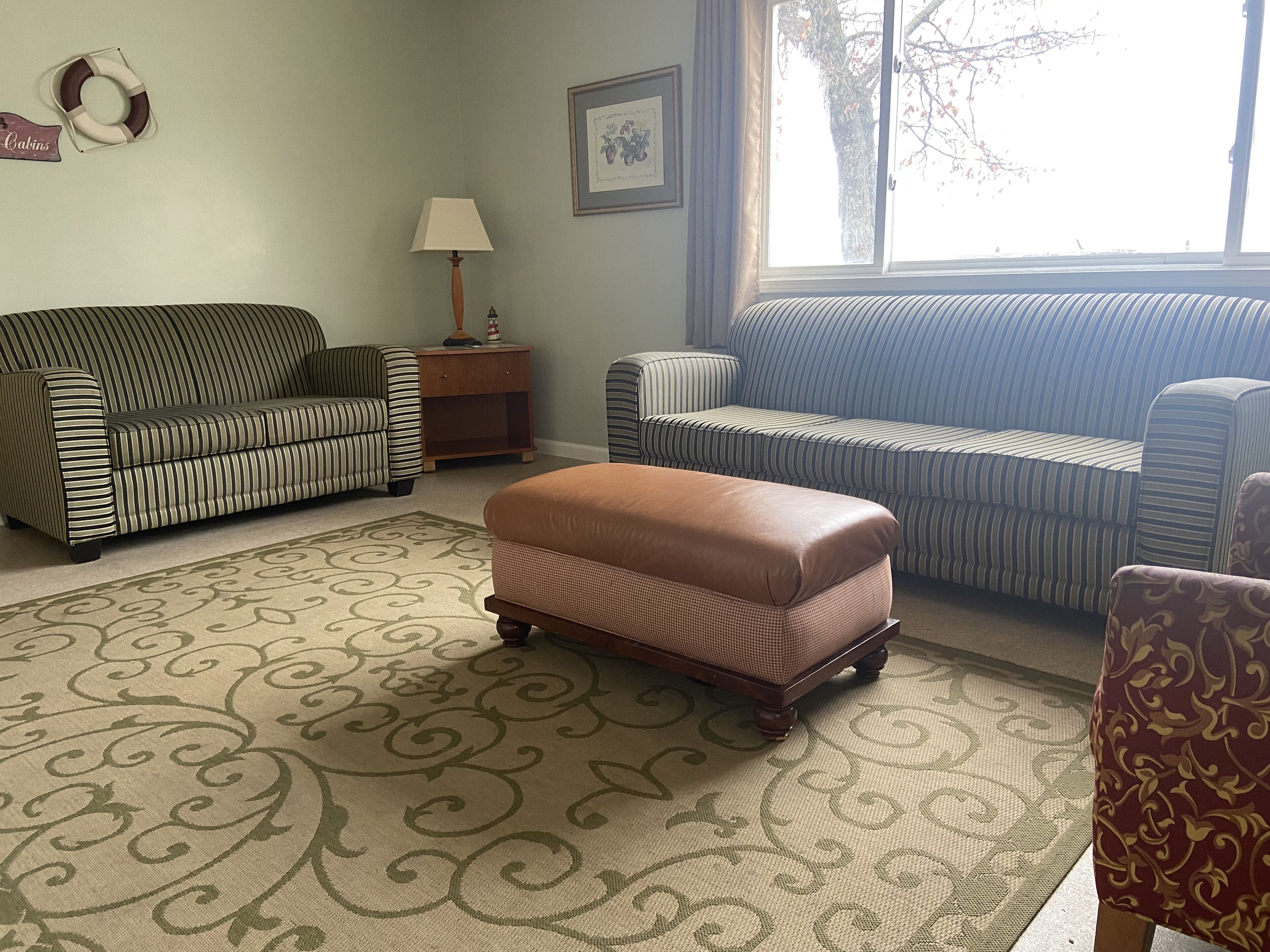 Un salon avec des canapés à rayures, un tapis à motifs et une petite table en bois sur laquelle se trouve une lampe.