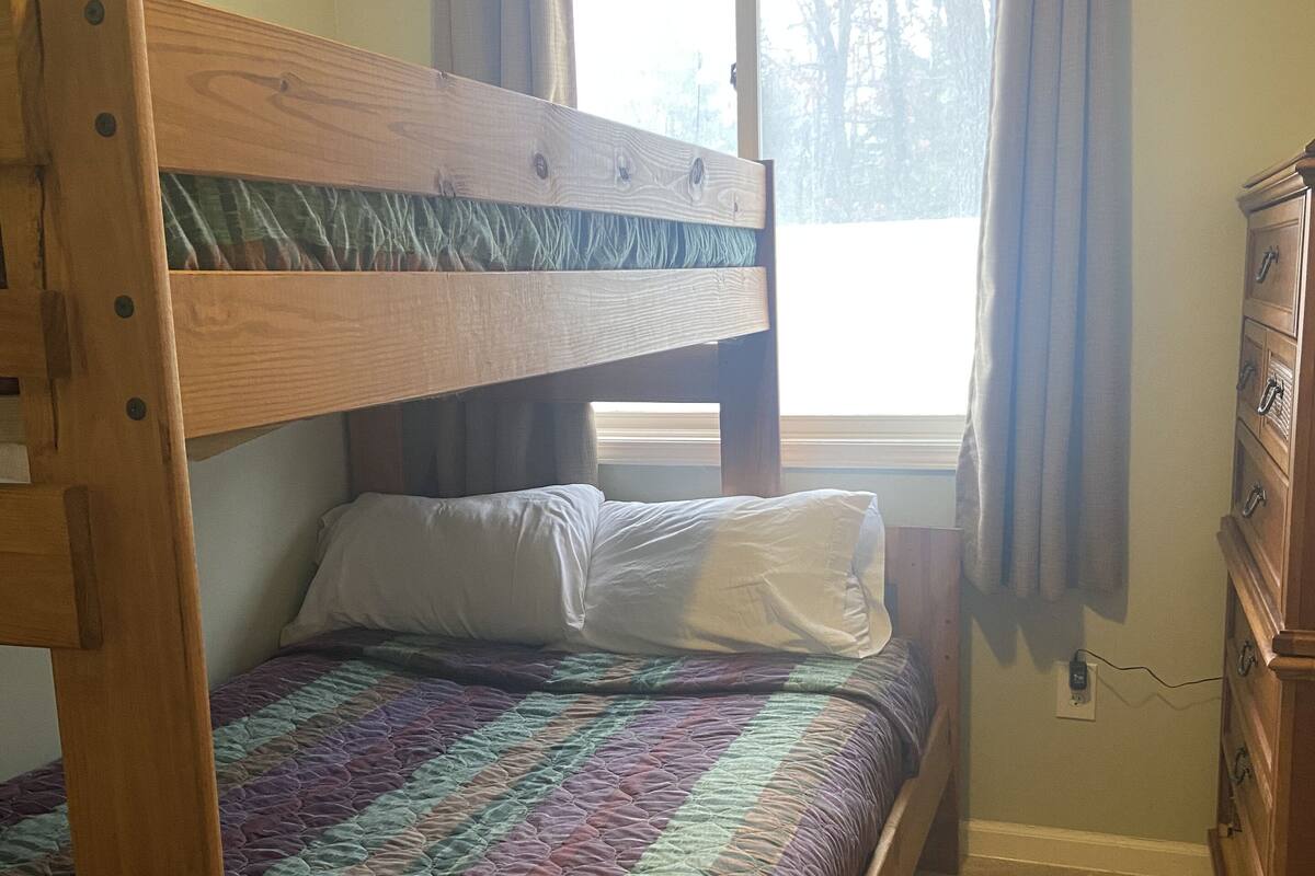 Una litera de madera individual con colcha acolchada, un aparador y una ventana con cortinas.