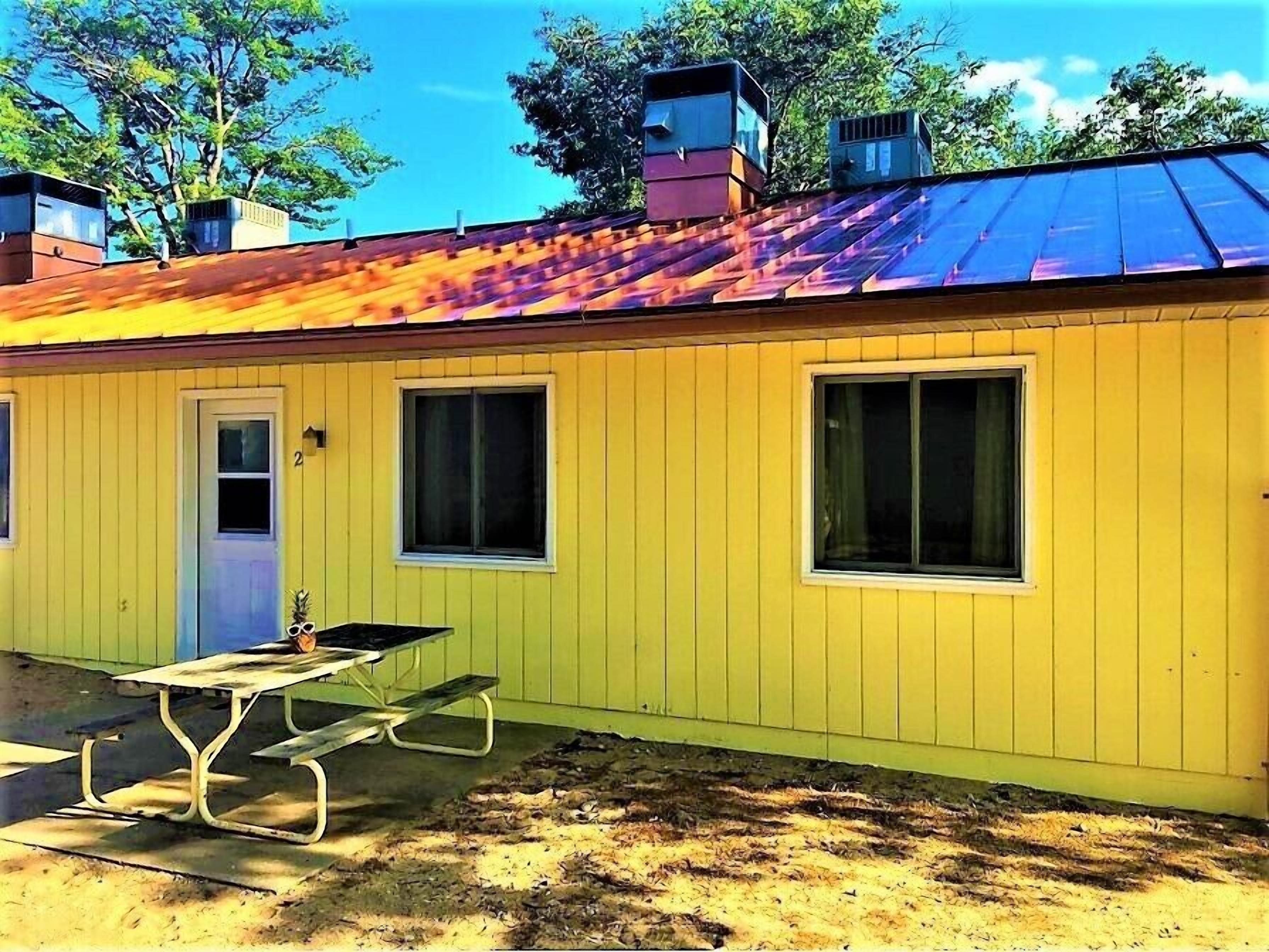A yellow building with a metal roof, two windows, and a door.
