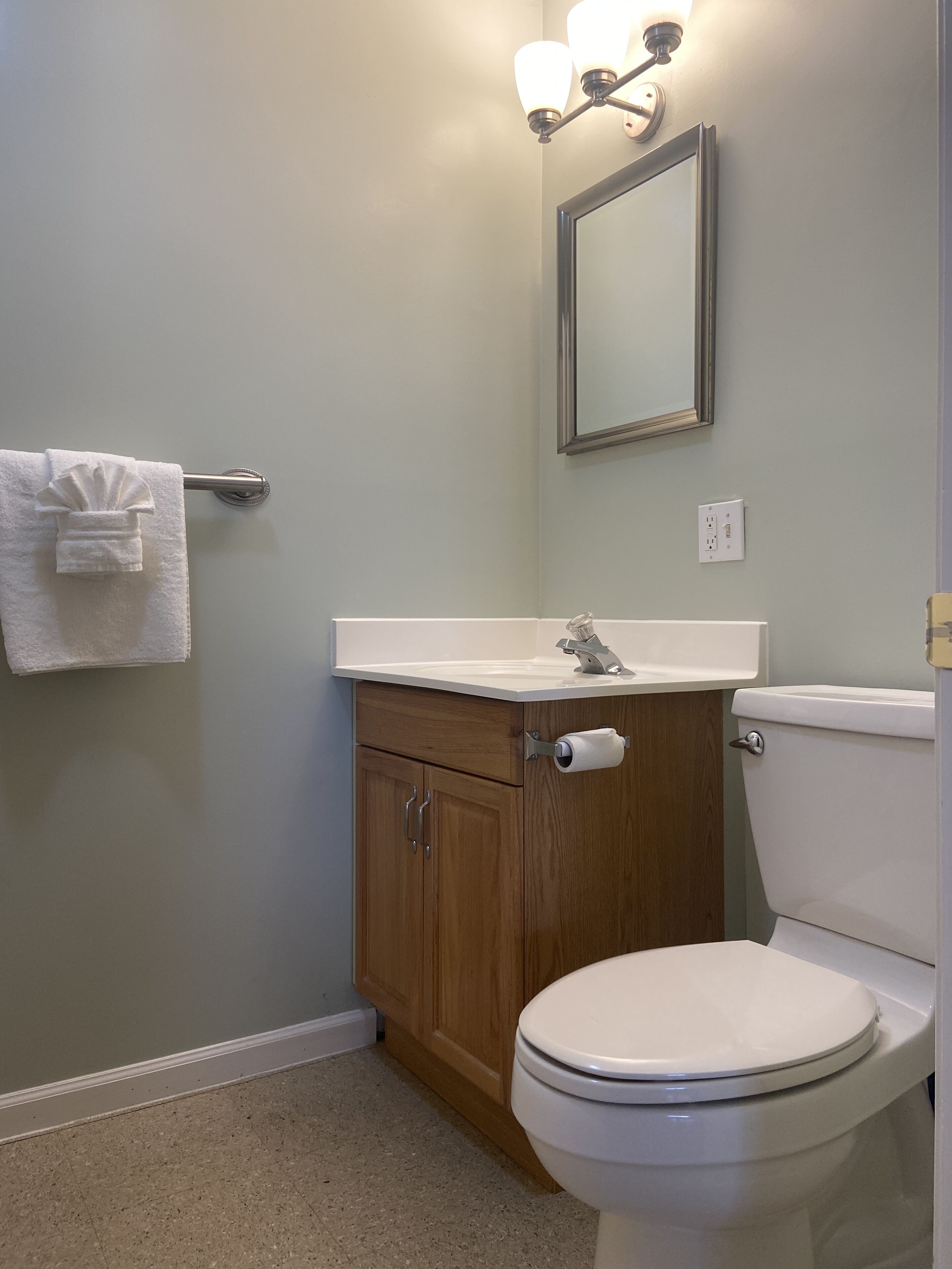 A bathroom with a toilet, a sink, a mirror, and a towel rack.