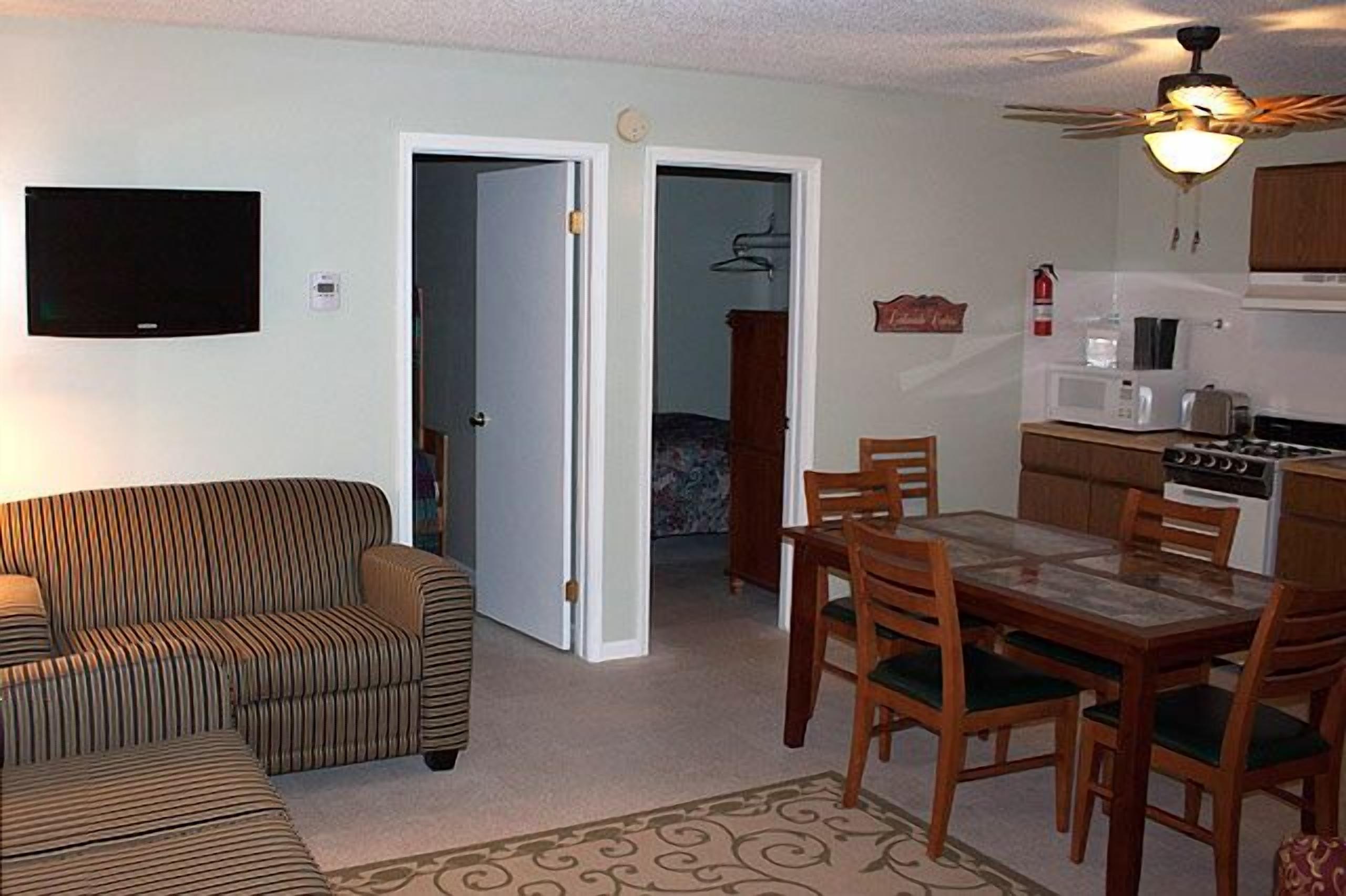Ein Wohnzimmer mit einer Couch, einem Esstisch mit Stühlen, einer Küchenzeile inklusive Herd und Mikrowelle sowie einem Deckenventilator.