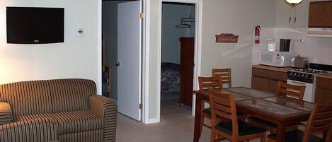 Ein Wohnzimmer mit einer Couch, einem Esstisch mit Stühlen, einer Küchenzeile inklusive Herd und Mikrowelle sowie einem Deckenventilator.