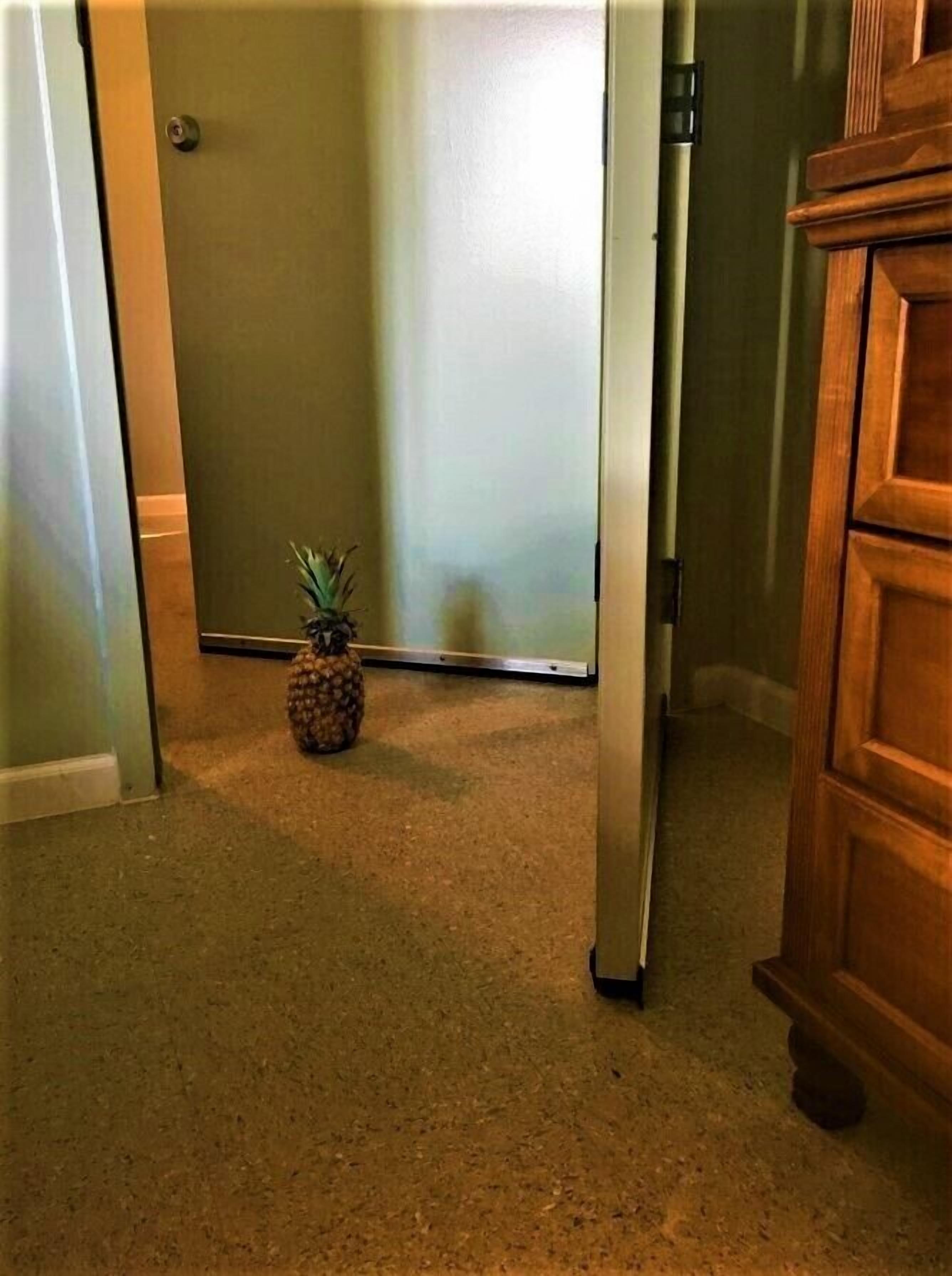 A hallway with a pineapple on the floor, a door, and a wooden cabinet.