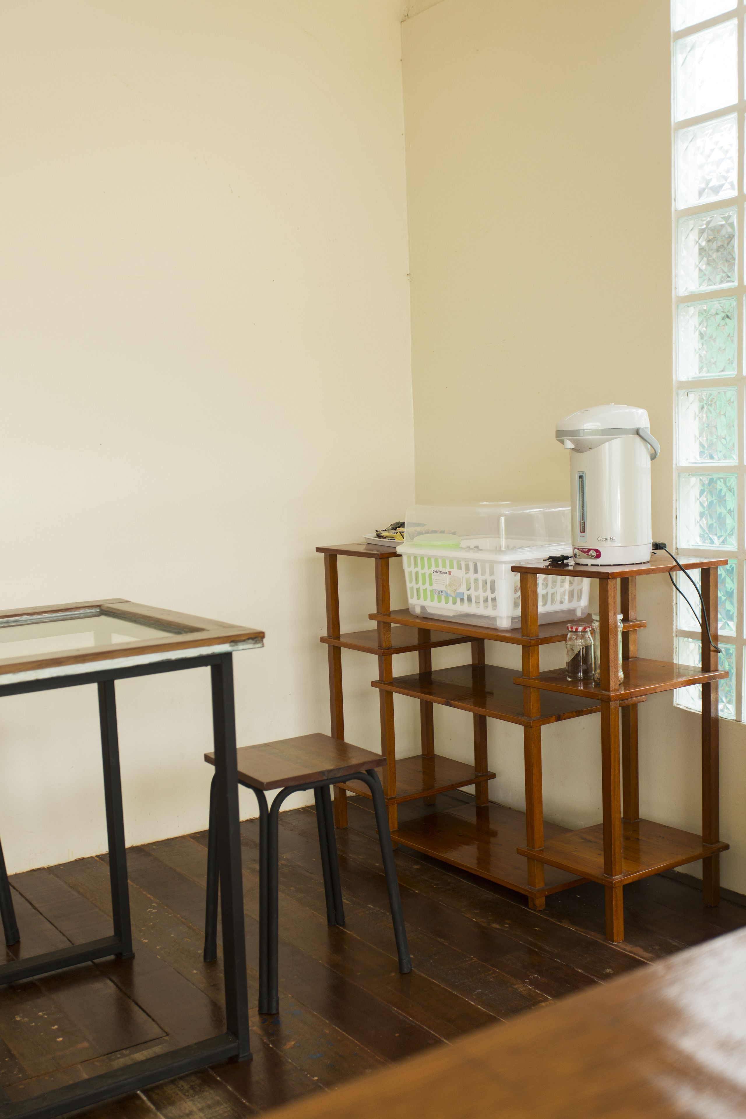 A room with a wooden table, a stool, and a shelf with a kettle and laundry basket.