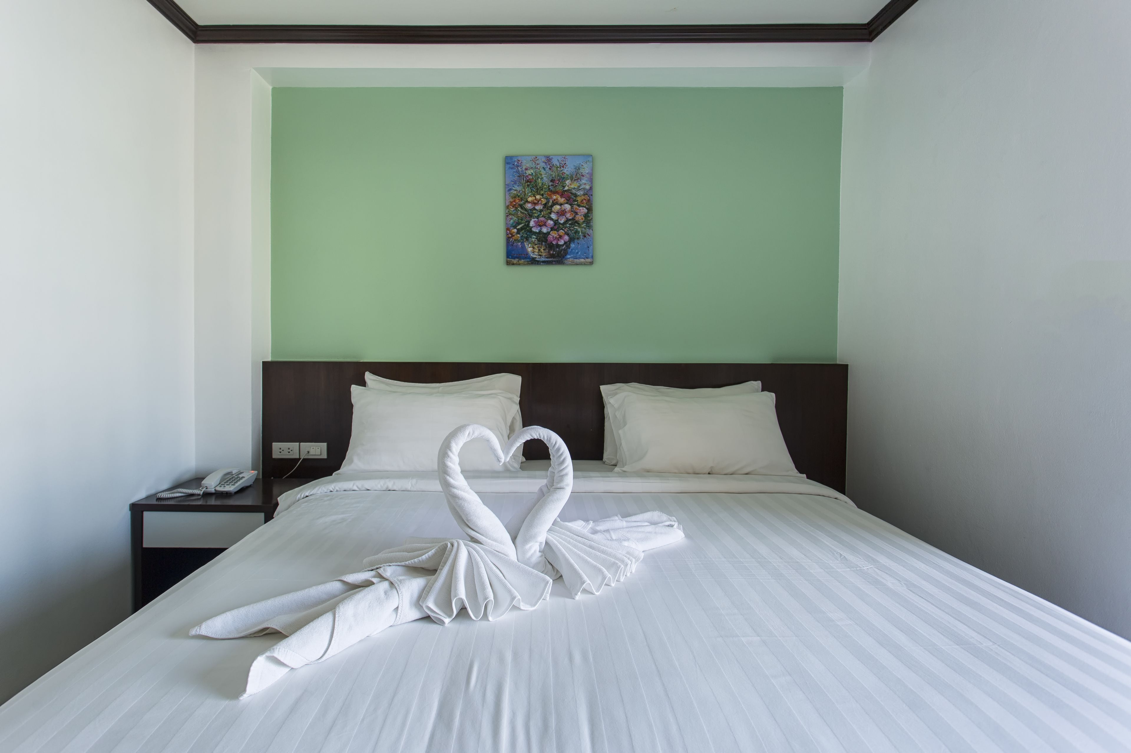 A hotel room with a bed, a nightstand, a painting on the wall, and a swan-shaped towel arrangement.