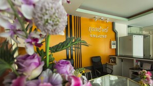 A modern hotel room with a glass table, a yellow accent wall, and a reception desk. - Kulasab Hotel (Hat Yai)