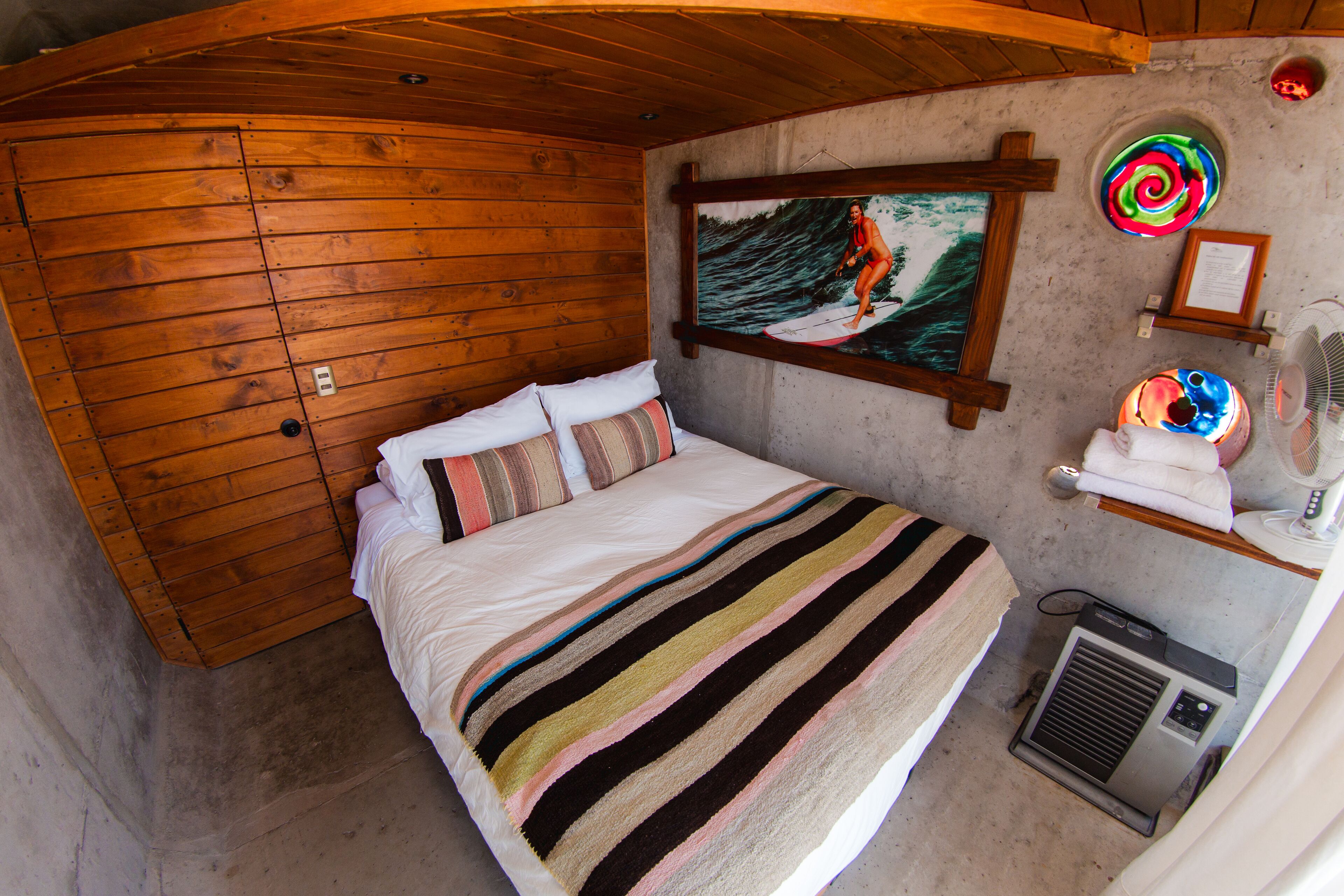 A wooden-paneled room with a bed, a painting, a fan, and a heater.