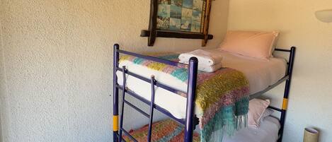 A bunk bed with a colorful blanket, a wooden ceiling, and a framed picture on the wall.