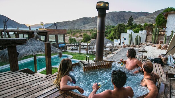 Et boblebadområde med en træterrasse, en swimmingpool og et bjerglandskab i baggrunden.