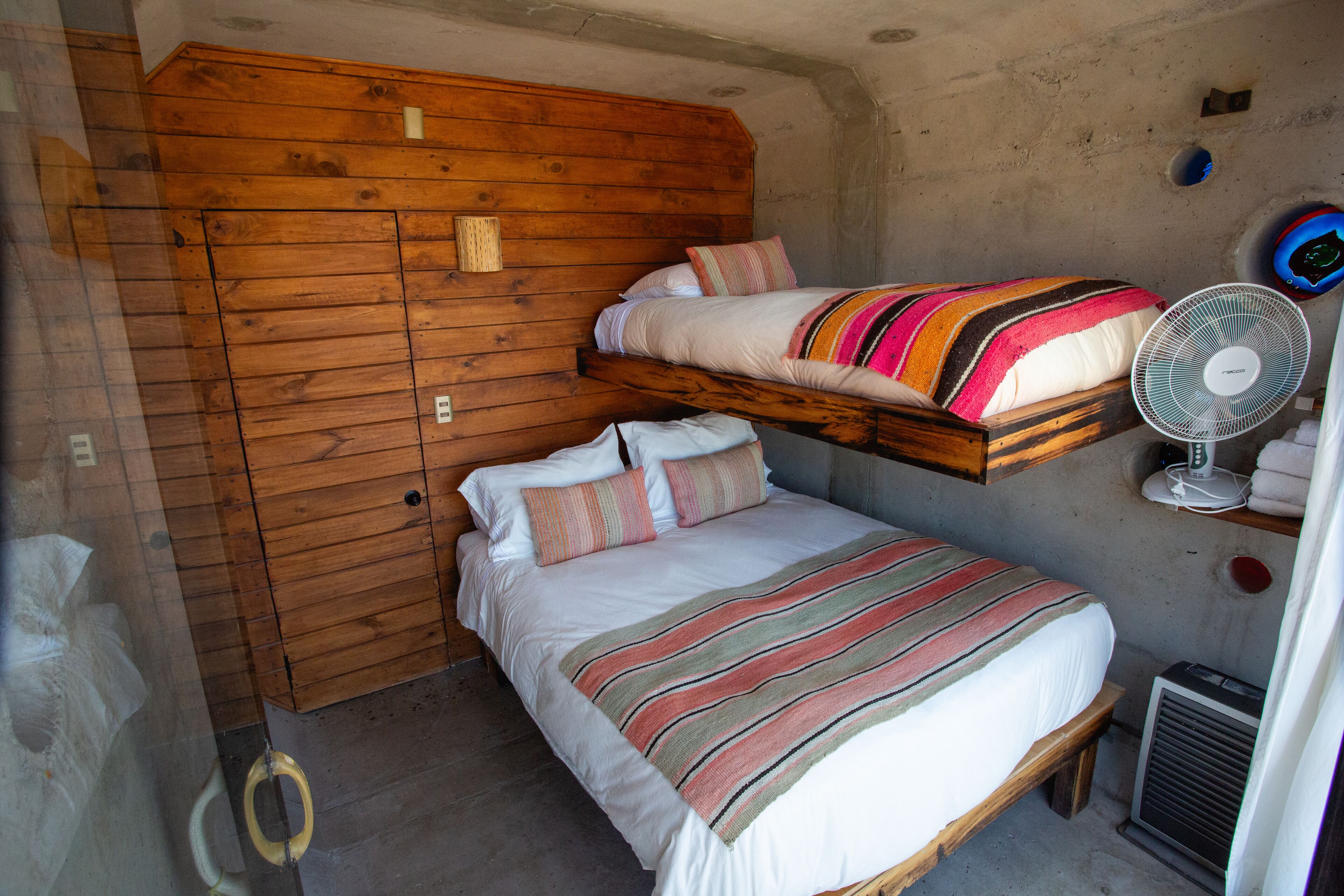 A bunk bed room with a wooden headboard, a standing fan, and a heater.