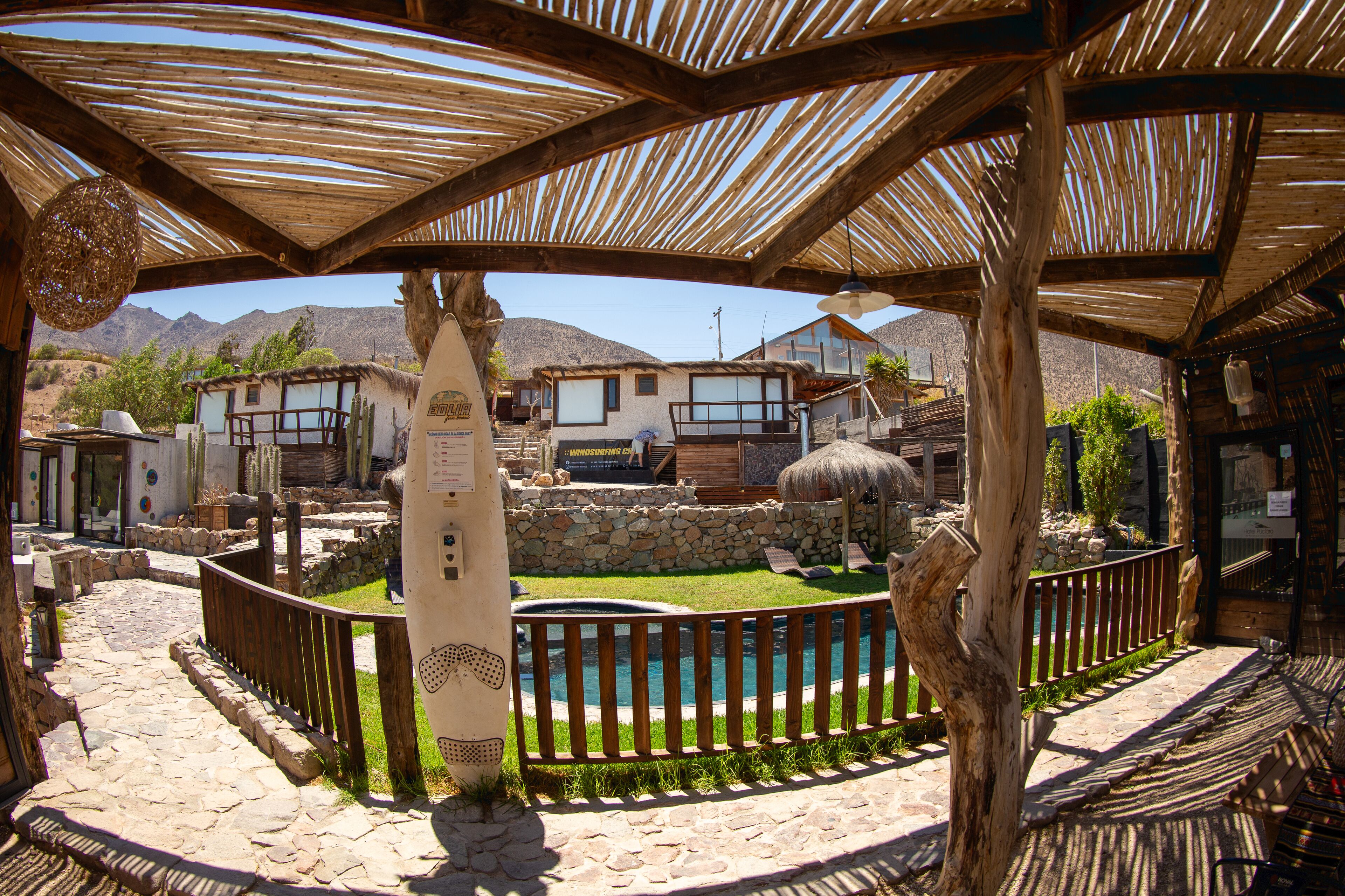 A wooden pergola with a pool and stone pathway, surrounded by rustic buildings and mountains in the background.