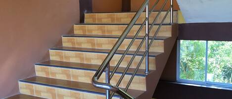 A staircase with wooden steps and metal railings, leading to a landing with a window overlooking greenery.