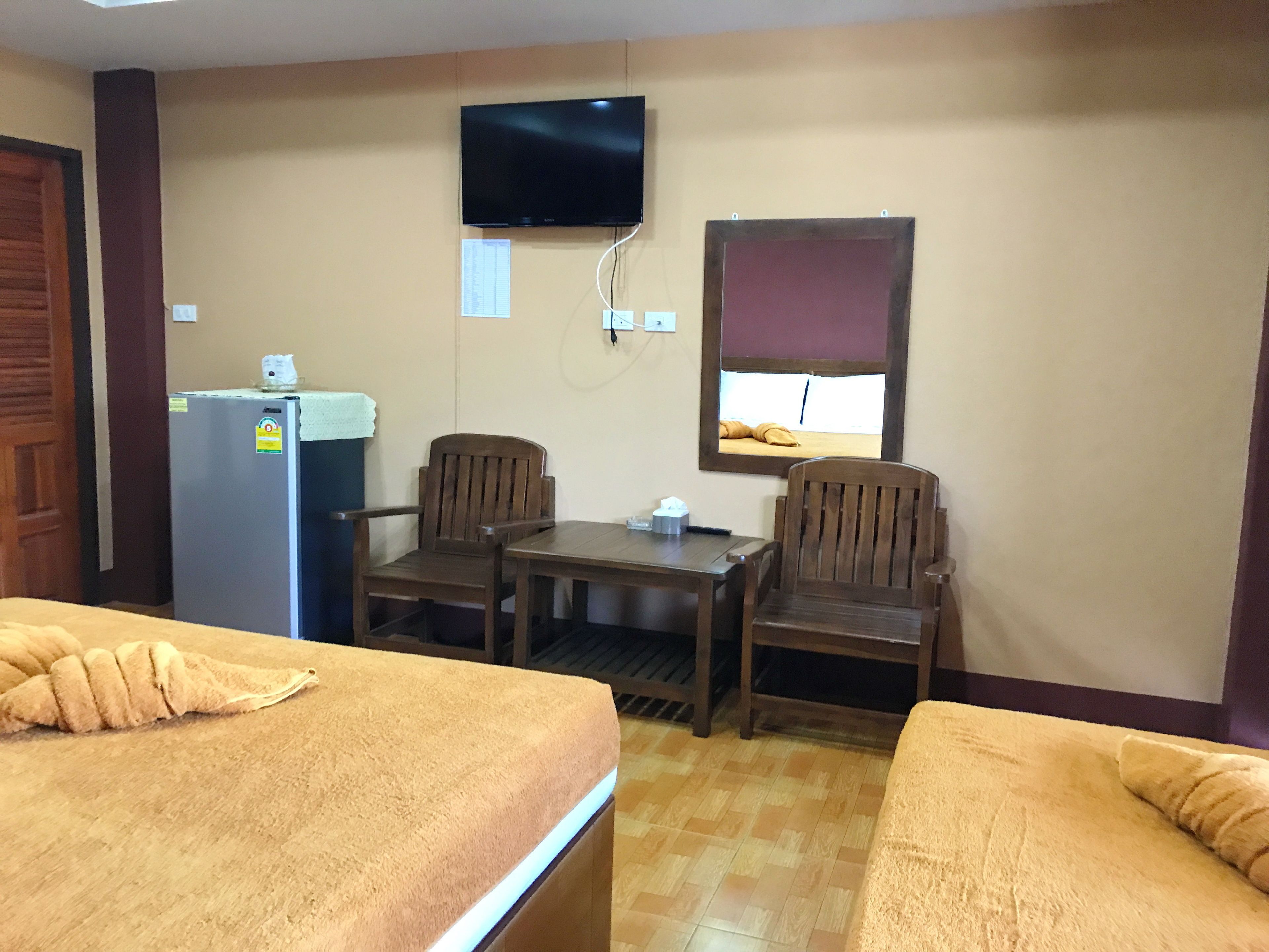 A hotel room with two beds, a small table, two chairs, a television mounted on the wall, a window with a blind, and a refrigerator.