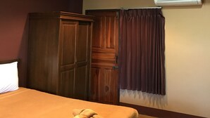 Une chambre à coucher comprenant un lit, une armoire en bois, un appareil de climatisation et une fenêtre avec des rideaux.