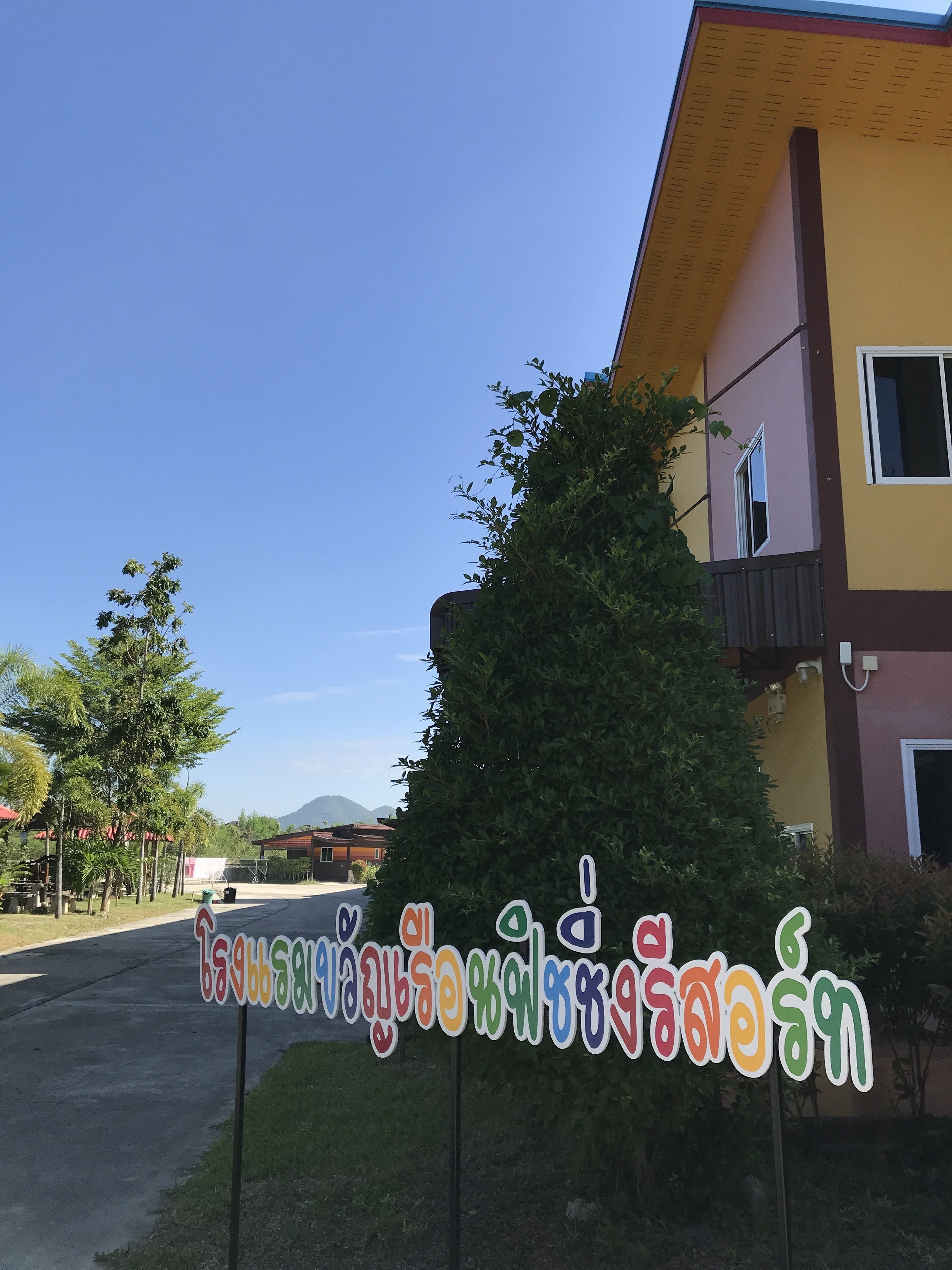 A sign with colorful text, a building with a yellow and brown facade, and a clear blue sky.