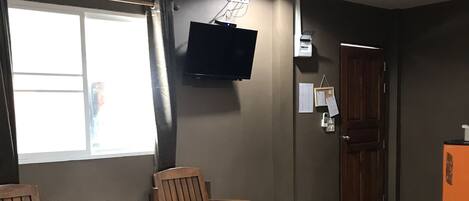 A hotel room with a bed, two wooden chairs, a small table, a TV mounted on the wall, and a window with curtains.
