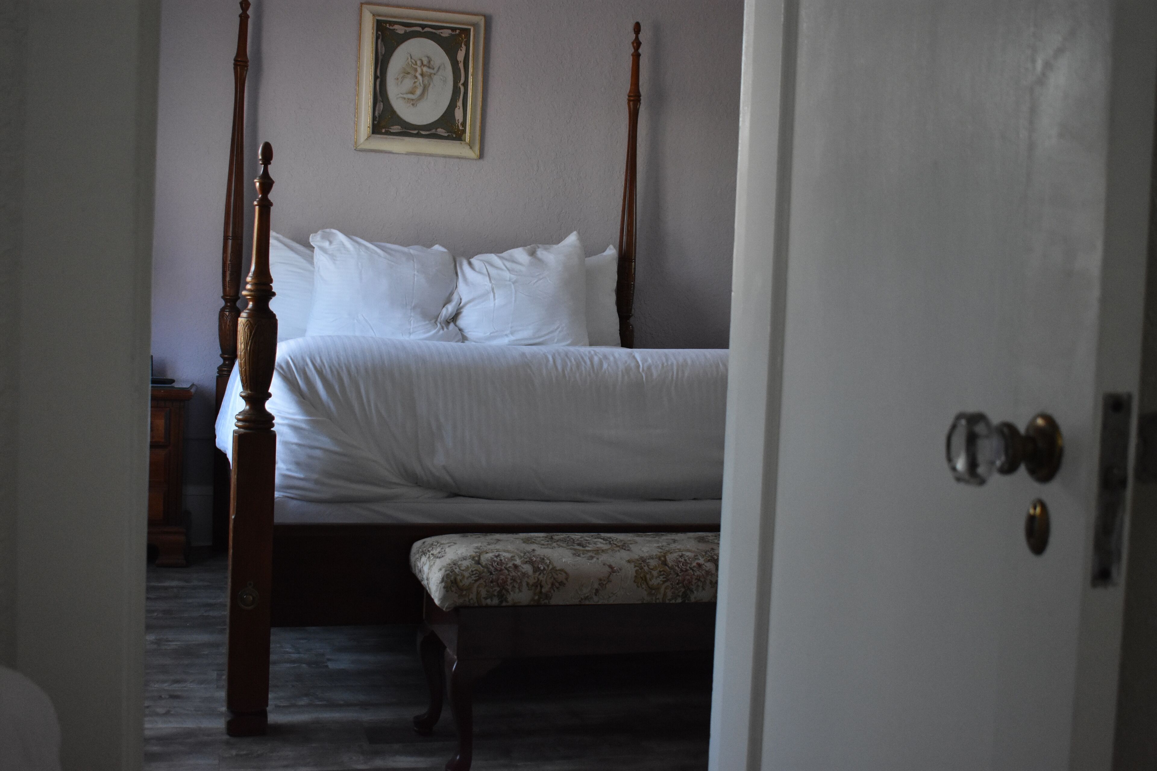 A bedroom with a four-poster bed, a bedside table, and a framed picture on the wall.