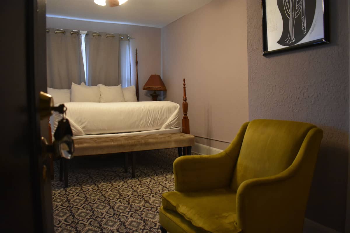 A hotel room with a bed, a bench, a lamp, and a chair.