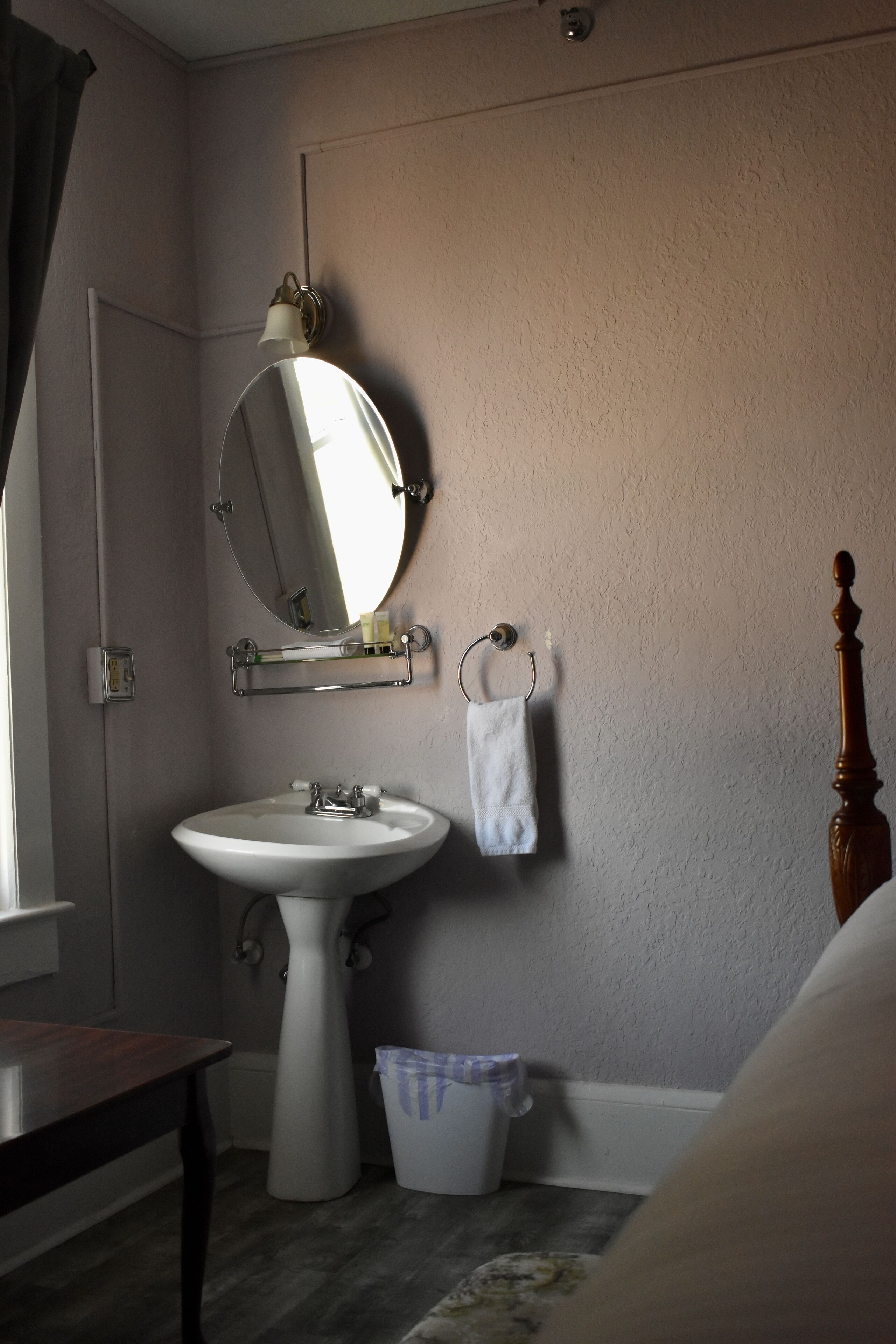 Um banheiro com pia de pedestal, espelho redondo, porta-toalhas e estrutura de cama de madeira.