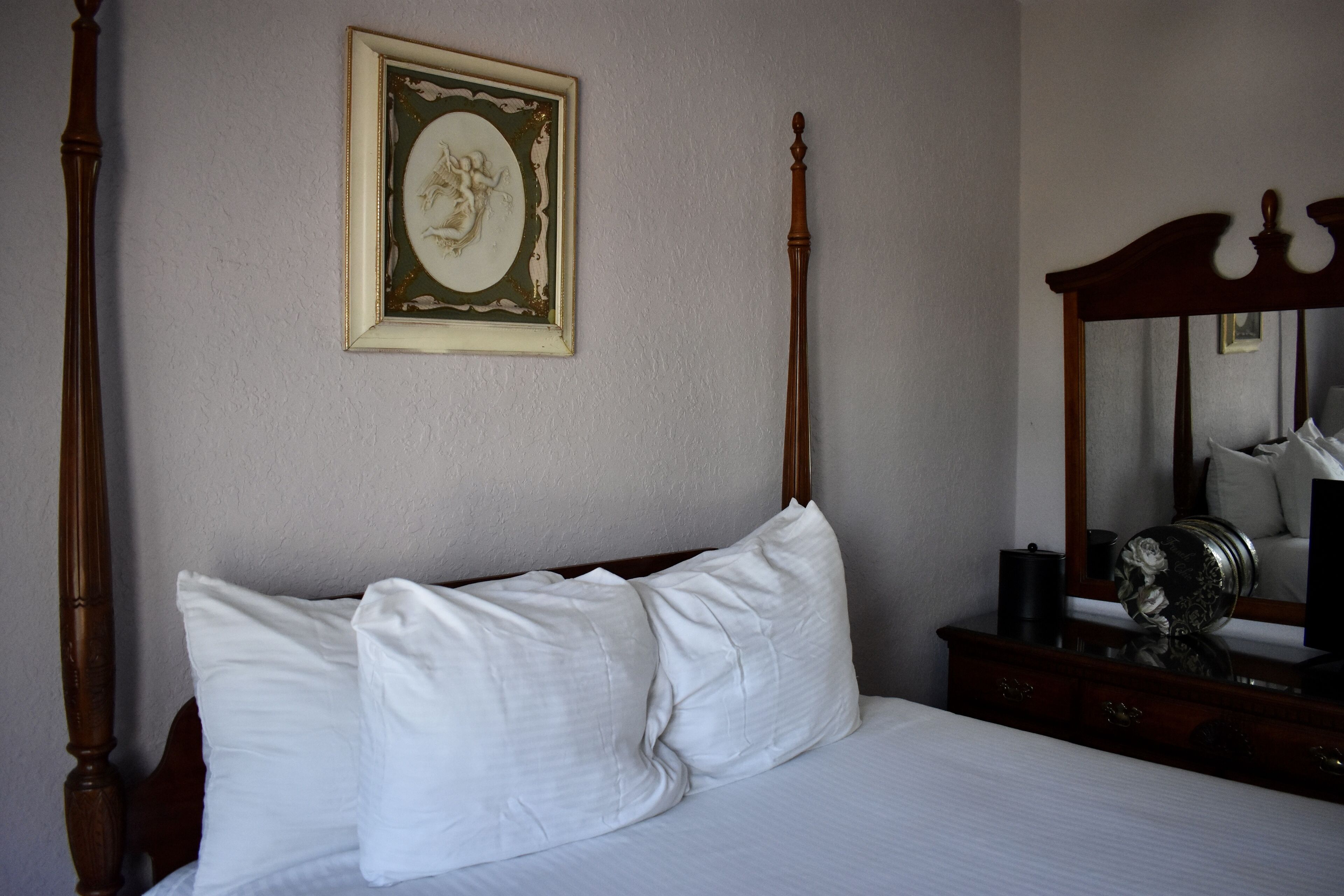A bedroom with a four-poster bed, a framed picture on the wall, and a dresser with a mirror.