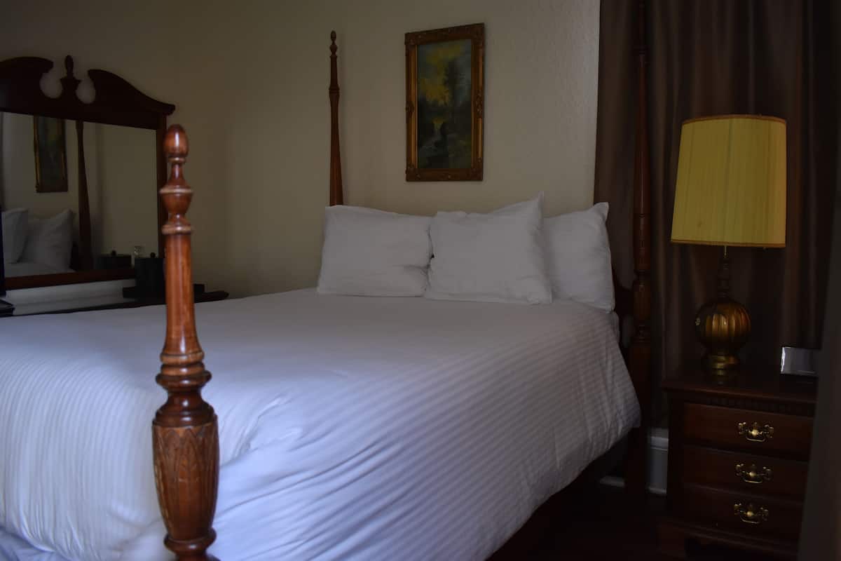 A neatly made bed with white linens, a wooden headboard, a bedside lamp, and a nightstand with drawers.