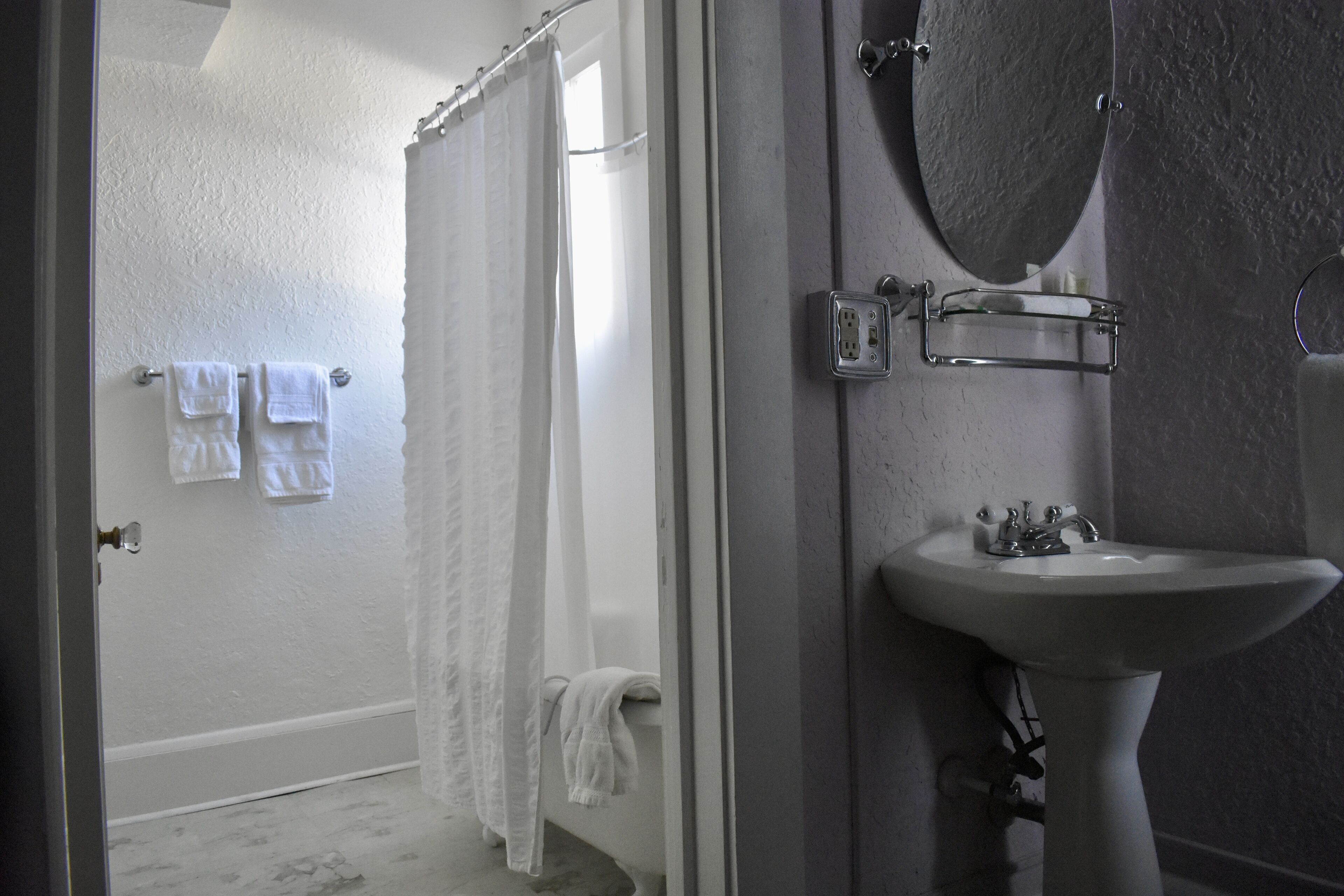Ein Badezimmer mit einer Badewanne, einem weißen Waschbecken, einem Spiegel und einem Handtuchhalter mit Handtüchern.